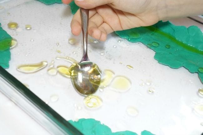 Sixth grade science student using a spoon to try to catch a puddle of oil floating on water