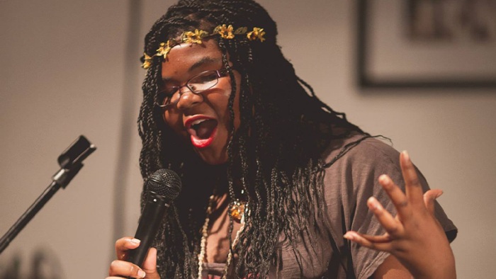 Black woman holding a microphone performing slam poetry