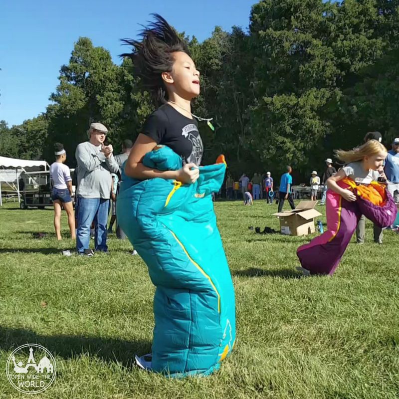 Girl competing in a sleeping bag race outside in grass.