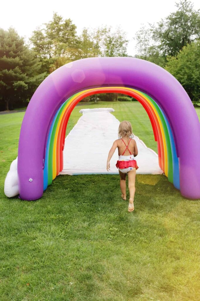 girl running through a blow up rainbow to a slip n slide for water activity