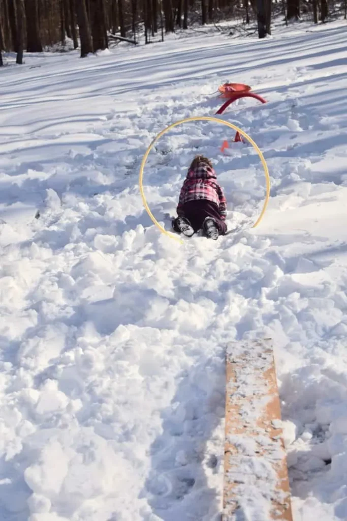 girl going through hoops in the snow for a fun winter activity snow obstacle course 