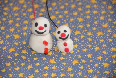 Two little play doh snowmen are attached by some simple wiring.