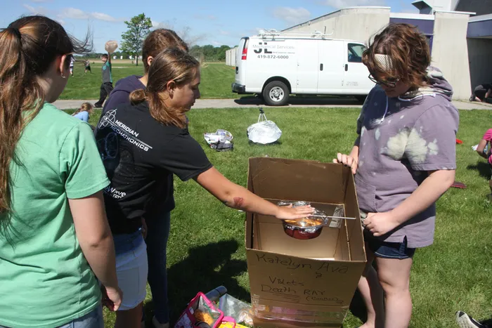 students cooking using a pizza box and mirror for a solar cookout