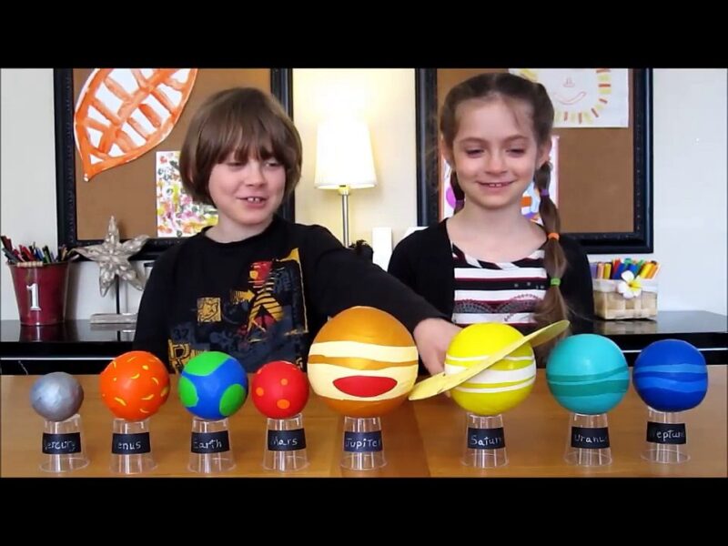 A little boy and a little girl stand behind models of all of the planets (solar system projects)