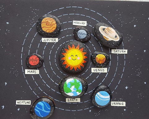 Rocks are painted to look like planets and the sun and are laid out on a black background (solar system projects)