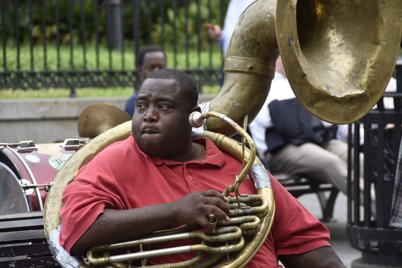 Black man in a red shirt sitting on a bench, wearing a sousaphone
