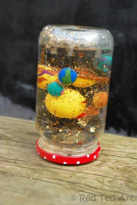 A snow globe made from an upside down jar has glitter and planets inside it (solar system planets)