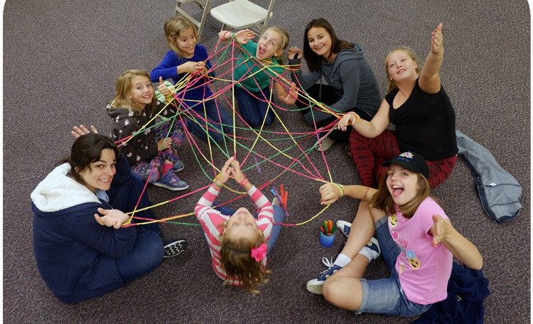 Students connected by a web of yarn sitting in a circle on the rug 