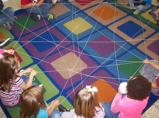 Students sitting in a circle around a colorful rug with a web made of yarn, as an example of icebreakers for kids