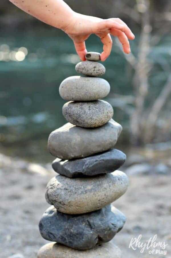 A small hand places a small stone at the top of a stack of rocks