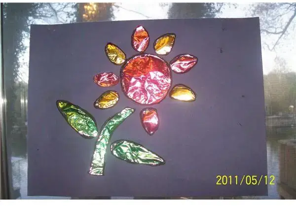 A flower is made from colored tin foil on a black background (spring crafts for kids)
