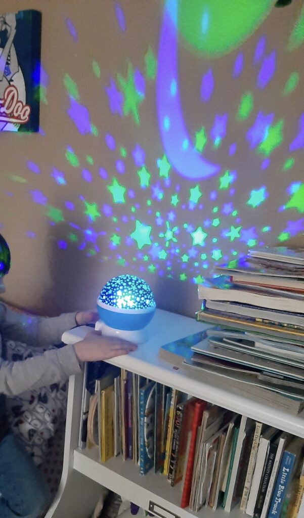 Child touching a star projector, which is sitting on top of a bookcase