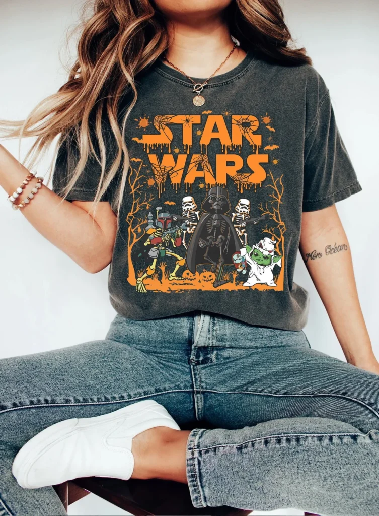 A seated woman is shown from the neck down wearing a dark gray shirt with orange letters that says Star Wars and Star Wars characters dressed for Halloween.