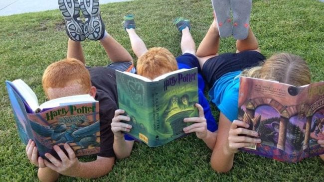 Three kids lying on the grass on their stomachs reading Harry Potter Books (Spring Break Activities)