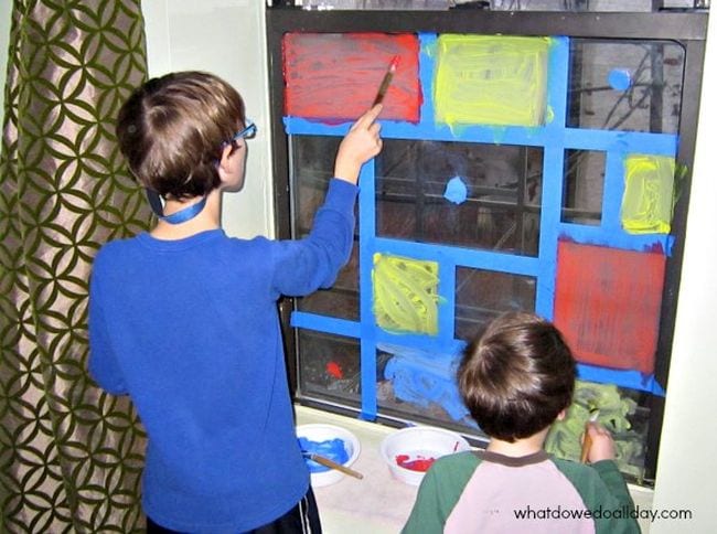 Two children painting colorful squares on a taped-off window
