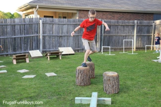 Boy running along tree stumps in a backyard