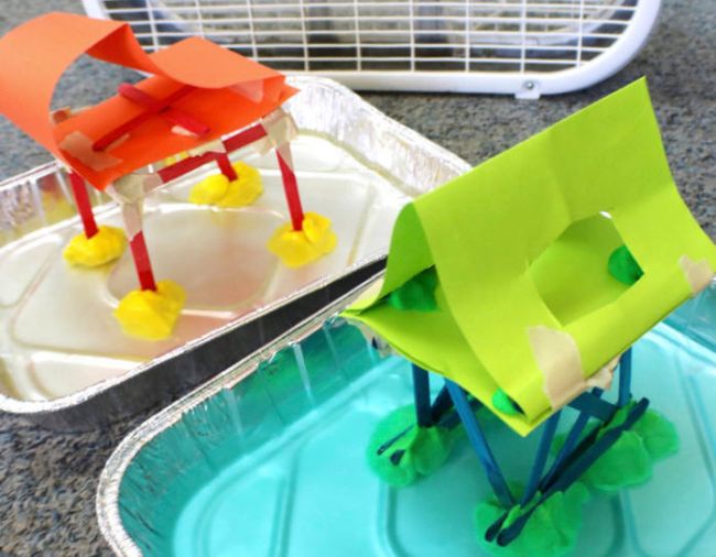 Two paper houses standing in tins of water with a fan in the background