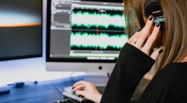 Student wearing headphones and using a computer to mix music