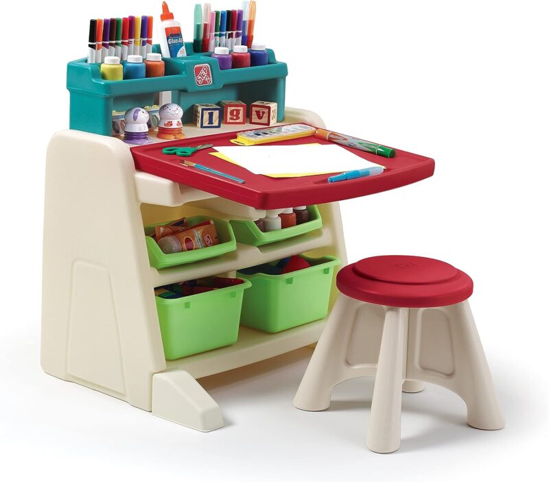 A plastic stand has storage above and below it filled with art supplies. A desk folds out from the center and a stool is in front of the desk. 