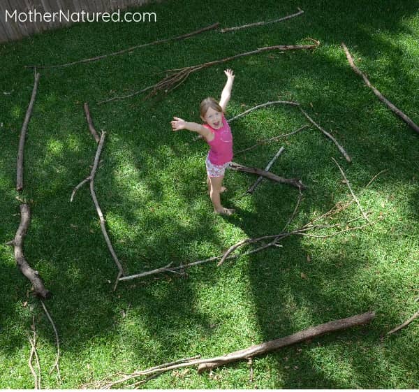 Girl standing in middle of a stick maze on the grass, as an example of camping activities for kids.