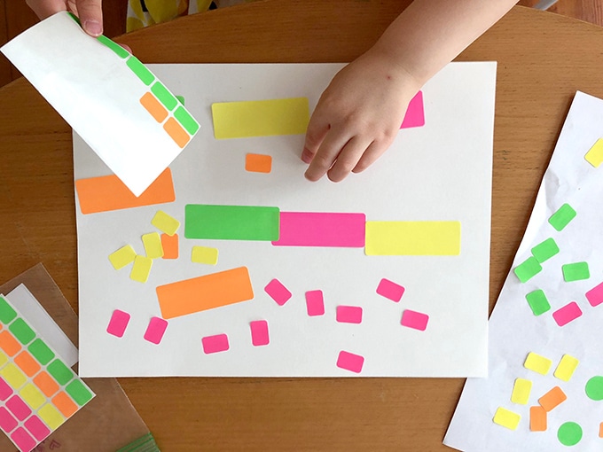 A child's hand is shown peeling stickers and placing them onto a piece of paper in this example of easy crafts for kids.