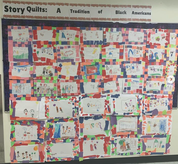 A bulletin board is covered in paper quilts made by students.