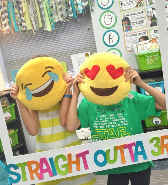 Students with emoji pillows over face posing in a classroom photo booth