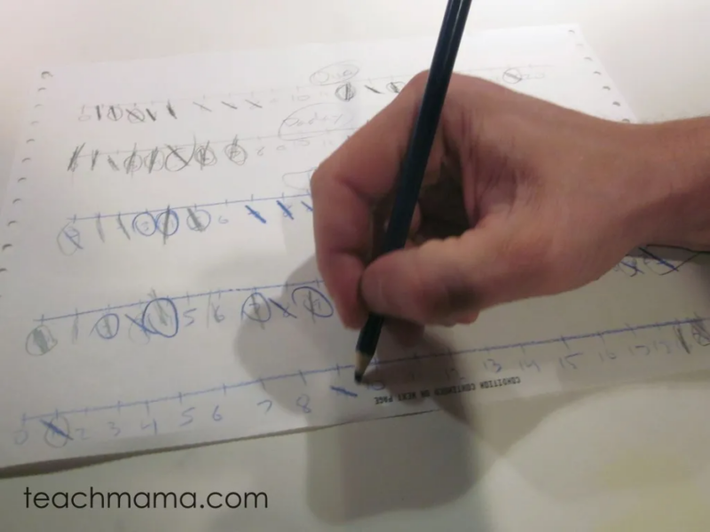 hand with pen writing on paper for a math fact game 