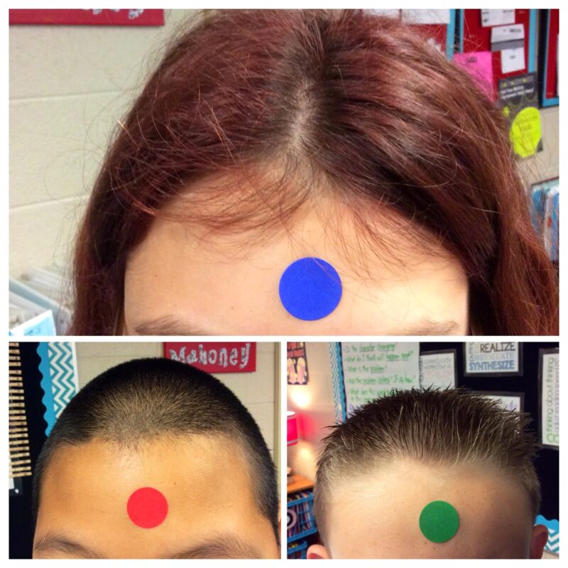 Three children's foreheads, each with a different colored stick on dot in the center as an example of team building activities for kids.