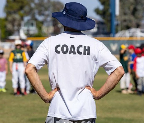 Coach standing with hands on hips in front of two young baseball teams