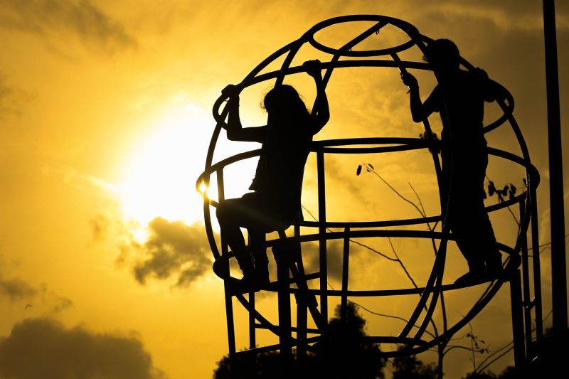 Two children on a jungle gym silhouetted against a setting sun