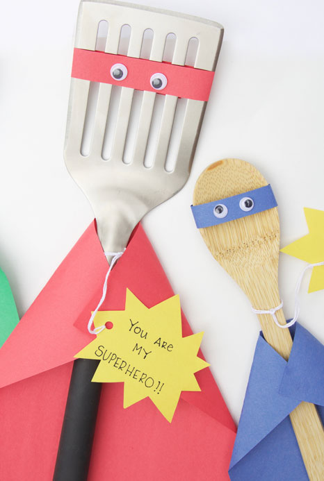 A spatula and a spoon are decorated to look like superheroes.