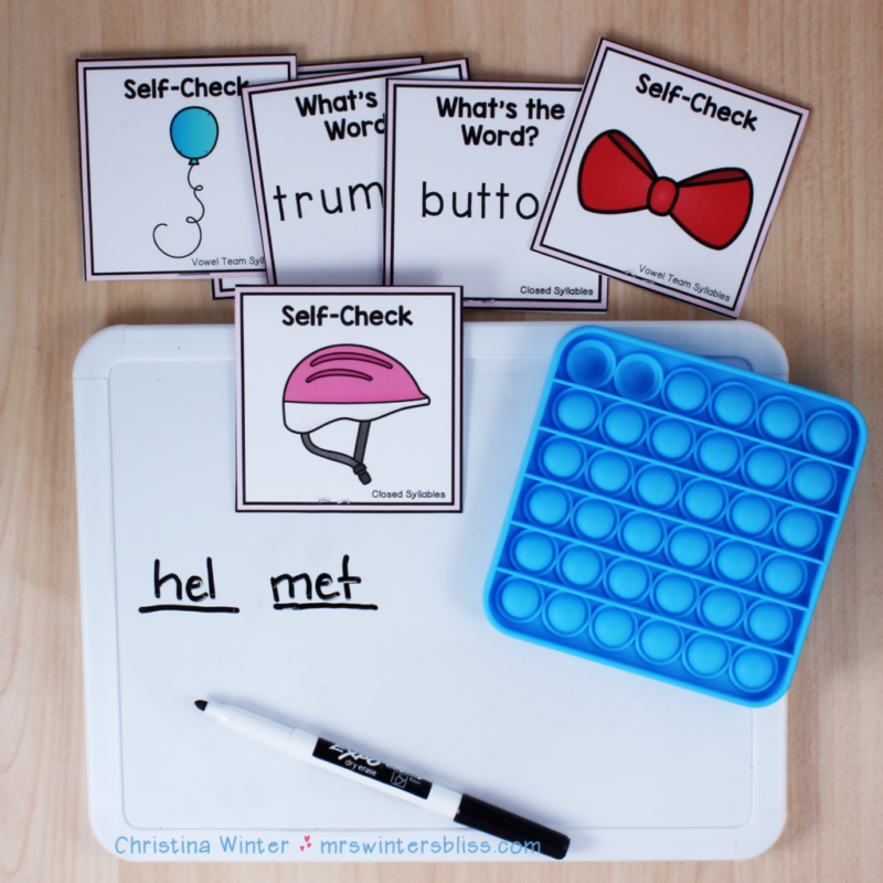 blue bubble popper with a whiteboard and black dry-erase marker, word cards, and the word "helmet" divided up into its two syllables, as an example of reading activities