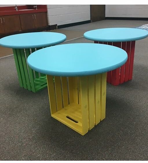 Several tables are made from crates turned on their side with blue round tops attached to the top.