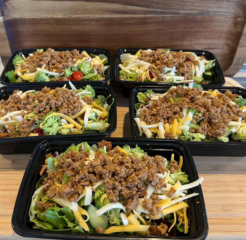 Five black plastic containers holding salad topped with spiced taco meat