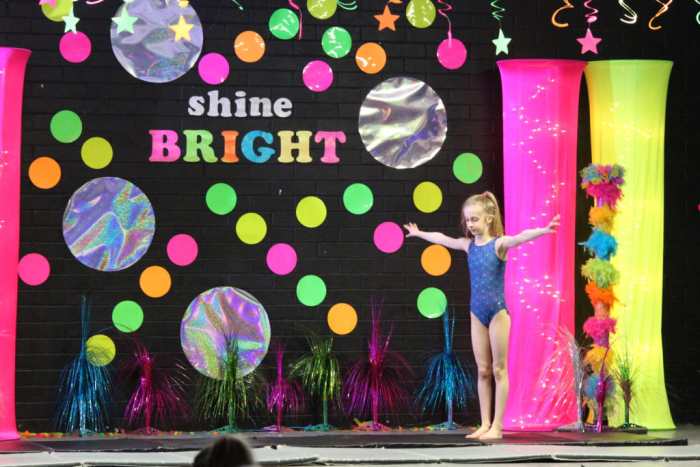 A student prepares to perform at a school talent show, against a brightly colored backdrop with text reading 