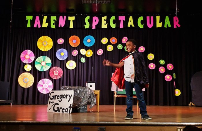 Student dressed in a black cape performing a magic trick in front of a display labeled 