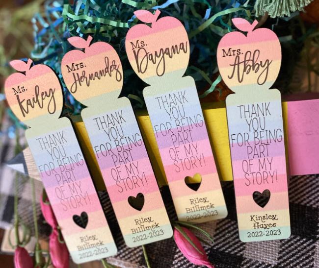 Pastel rainbow wooden bookmarks with an apple silhouette on top, reading "Thank you for being part of my story" and personalized with names as teacher appreciation gifts