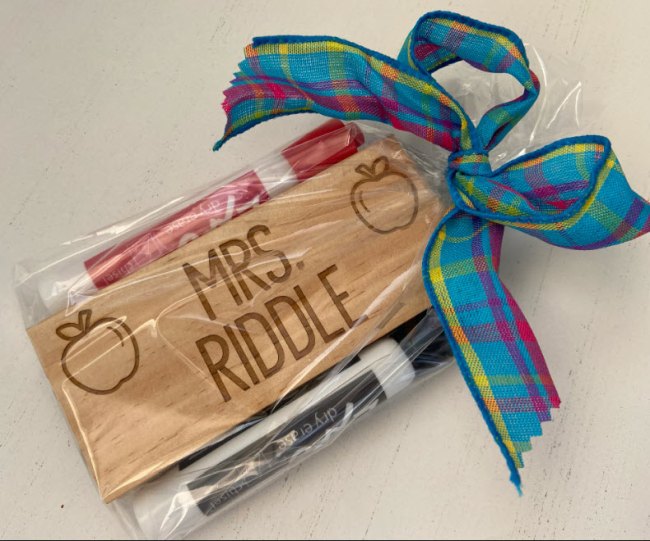 A personalized eraser for a dry erase board, wrapped in a cellophane bag with two dry erase markers and tied with a blue plaid bow