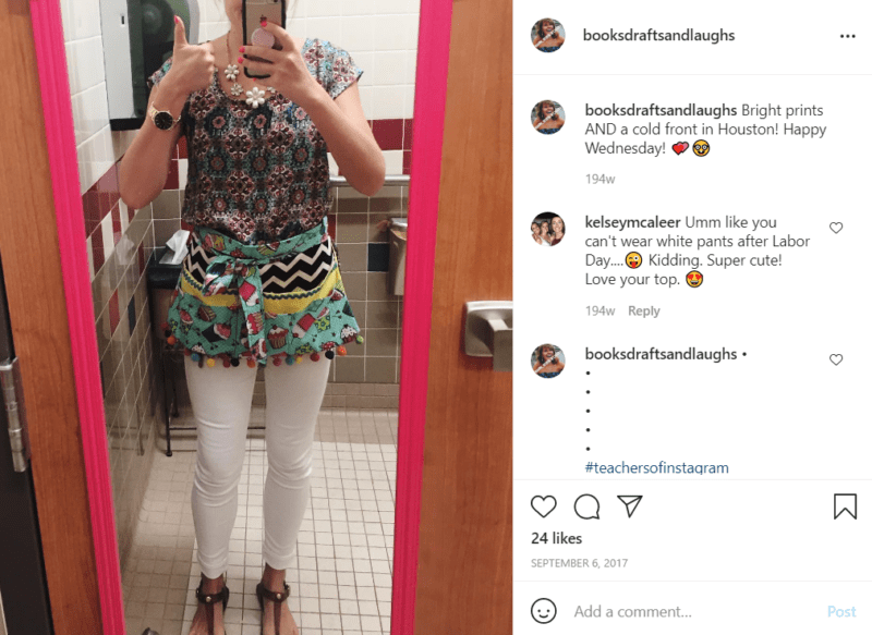 A woman taking a picture of herself in a mirror while wearing a teacher apron that has lots of dangly bits and accessories