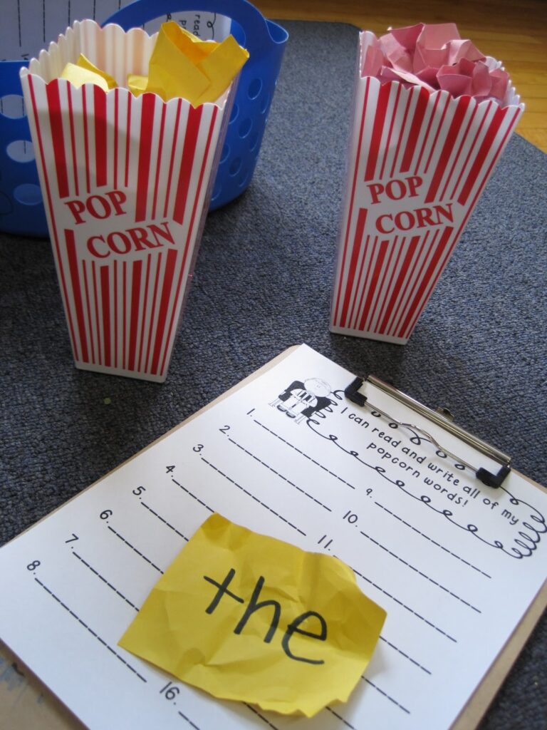 Red and white striped popcorn boxes with crumpled up paper inside of them next to a clipboard with a worksheet and the word "the" on a piece of yellow construction paper