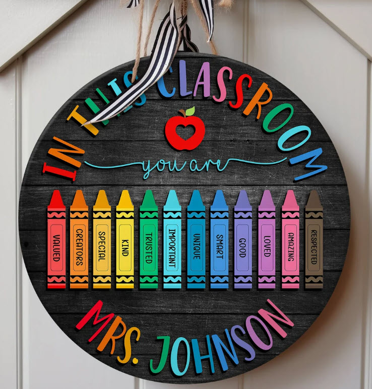 Round black sign with colorful crayons and a teacher's name