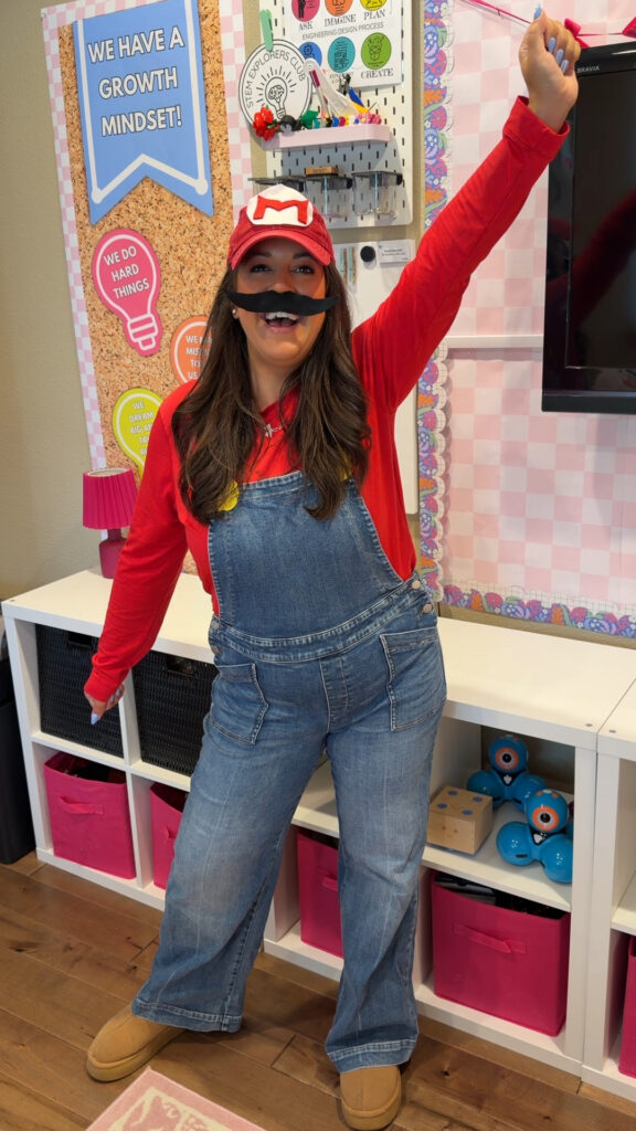 A teacher wears a red long-sleeved short with overalls and brown boots. She also wears a fake mustache and a red hat with the Super Mario logo on it.