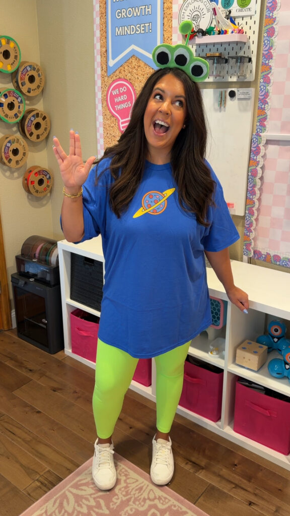A teacher wears a blue t-shirt with a Pizza Planet logo with lime green leggings and a headband with three monster eyes.