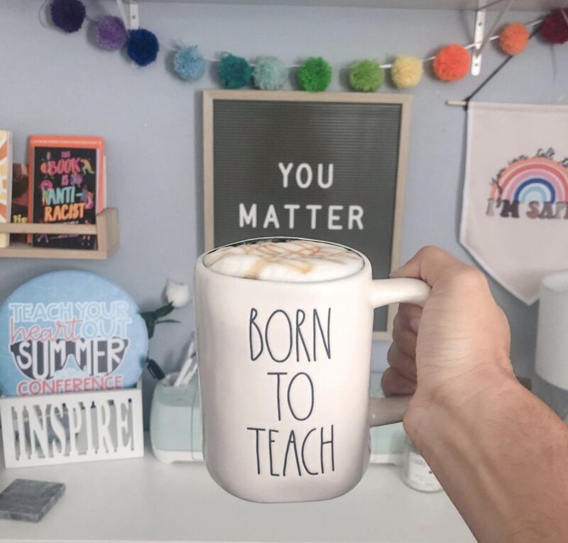 Hand holding a "Born to Teach" coffee mug