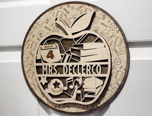Laser cut sign of balsa wood in the shape of an apple, with a teacher's name and various symbols of education (Teacher Name Signs)