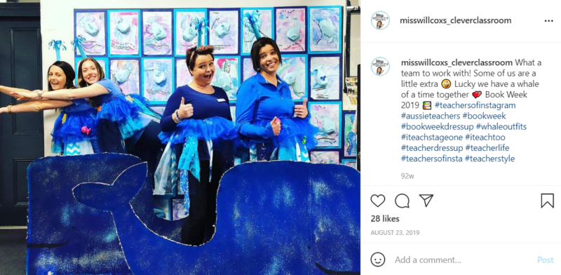 Four teachers wearing blue whale costumes in a classroom behind a cardboard cutout of a whale