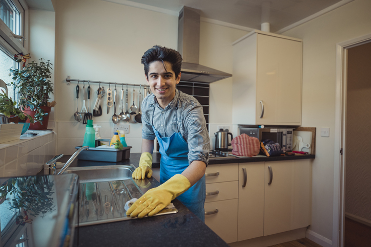 Teenage boy is smiling for the camera while cleaning a kitchen.