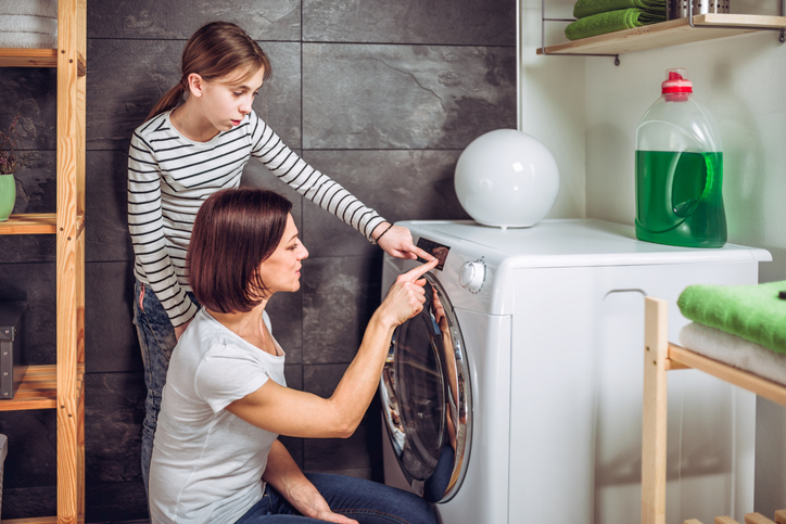 Mother and daughter selecting program on washing machine at laundry room, as an example of life skills for teens