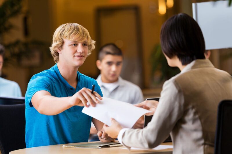 teen learning job readiness skills hands his resume across the table to a person conducting a mock interview 